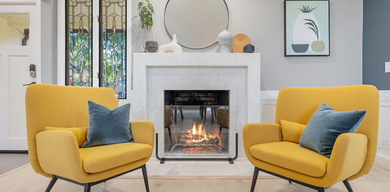 evoke-interior-designs-sacramento-ca-should-you-renovate-or-furnish-your-home-sitting-area-bold-yellow-chairs-by-fireplace-round-mirror-modern-art-personal-residential-interior-design