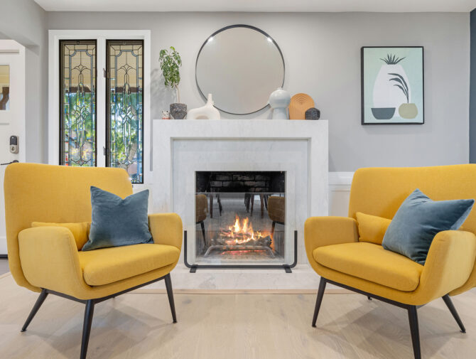 evoke-interior-designs-sacramento-ca-should-you-renovate-or-furnish-your-home-sitting-area-bold-yellow-chairs-by-fireplace-round-mirror-modern-art-personal-residential-interior-design